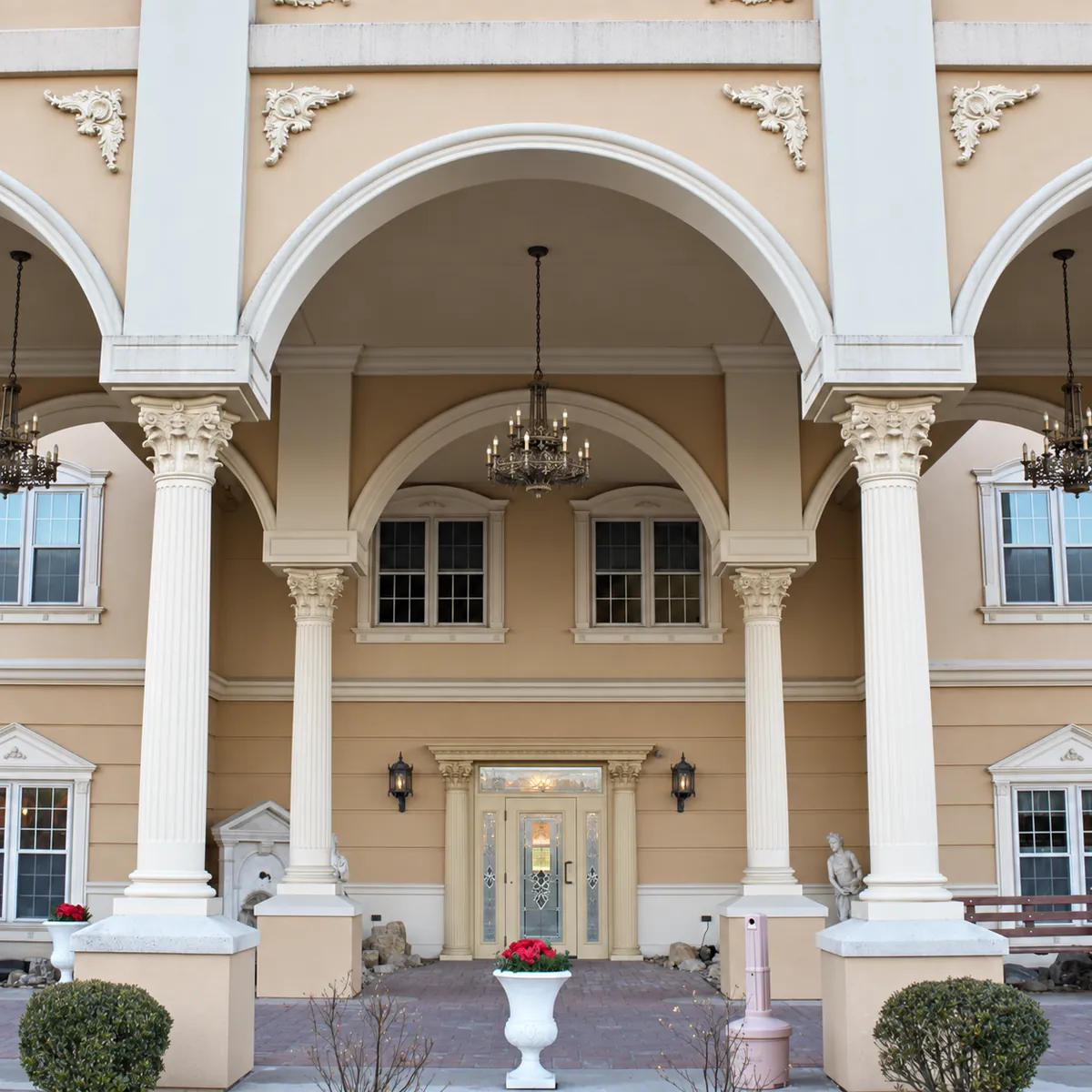 Entrance of Graystone Court Villas, a tan building with white columns, arches, and chandeliers, where Nu Look Salon is located